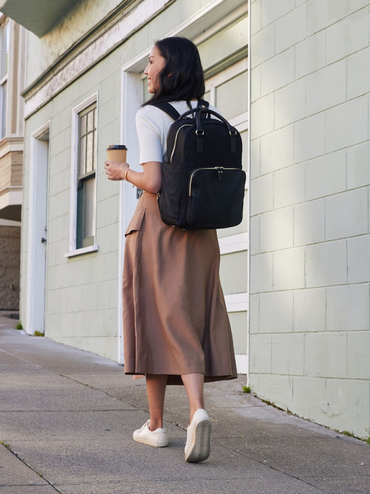Woman carrying in her hands a Lo & Sons Rowledge 2 backpack walking down the sidewalk in gym outfit