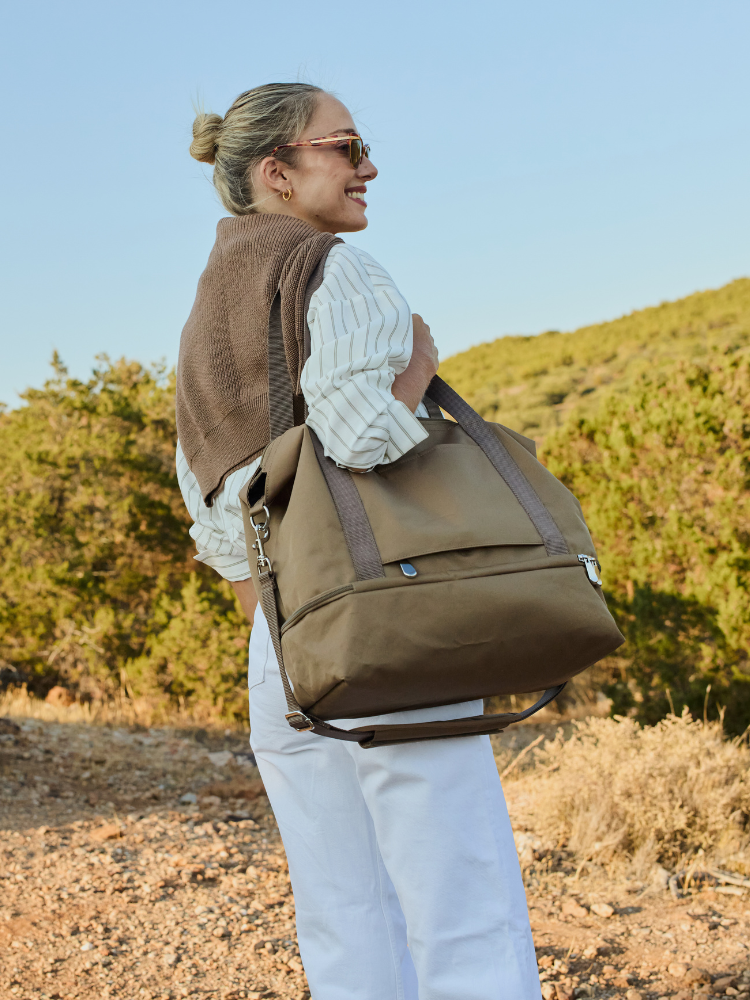 Woman standing in bedroom with the Lo & Sons Del Mar Packable Tote on her shoulder