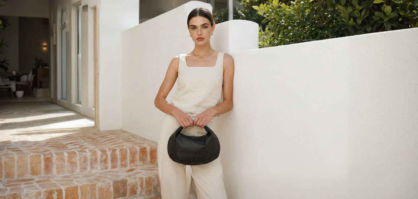 Woman in a white outfit holding a black Aoyama 2 in leather against a white wall.