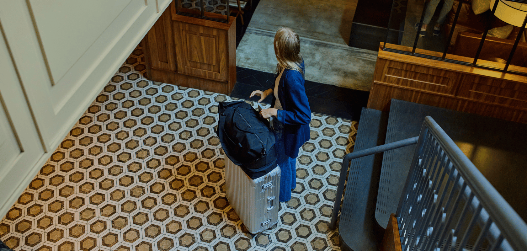 Woman with a Lo & Sons black Catalina Deluxe weekender duffel bag on top of a suitcase entering a hotel lobby