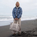woman in puffer jacket and hoodie on a beach in the winter time holding the Lo & Sons Catalina Deluxe in Dove Grey canvas 