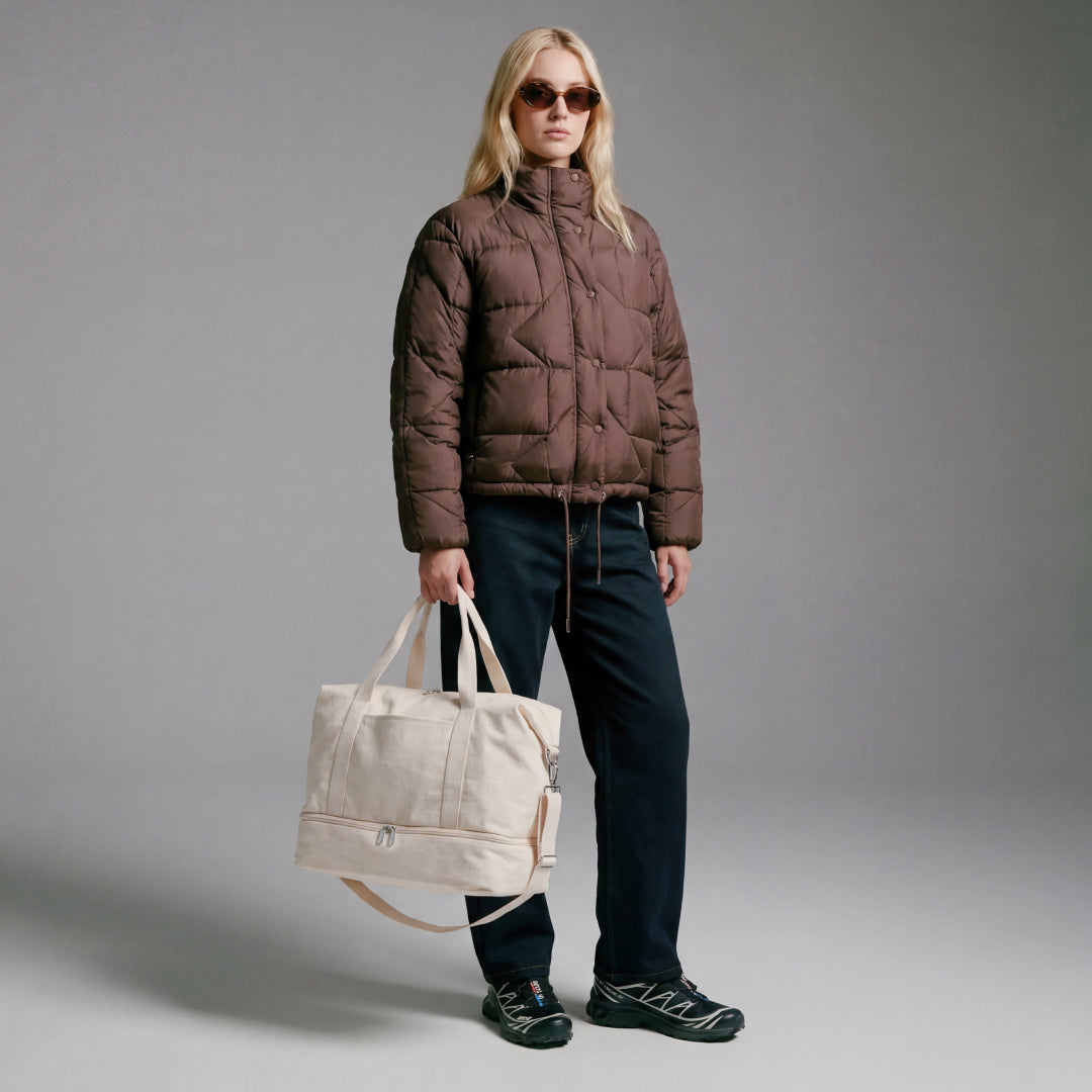 woman in puffer jacket and dark denim holding a Lo & Sons Catalina Deluxe in natural canvas
