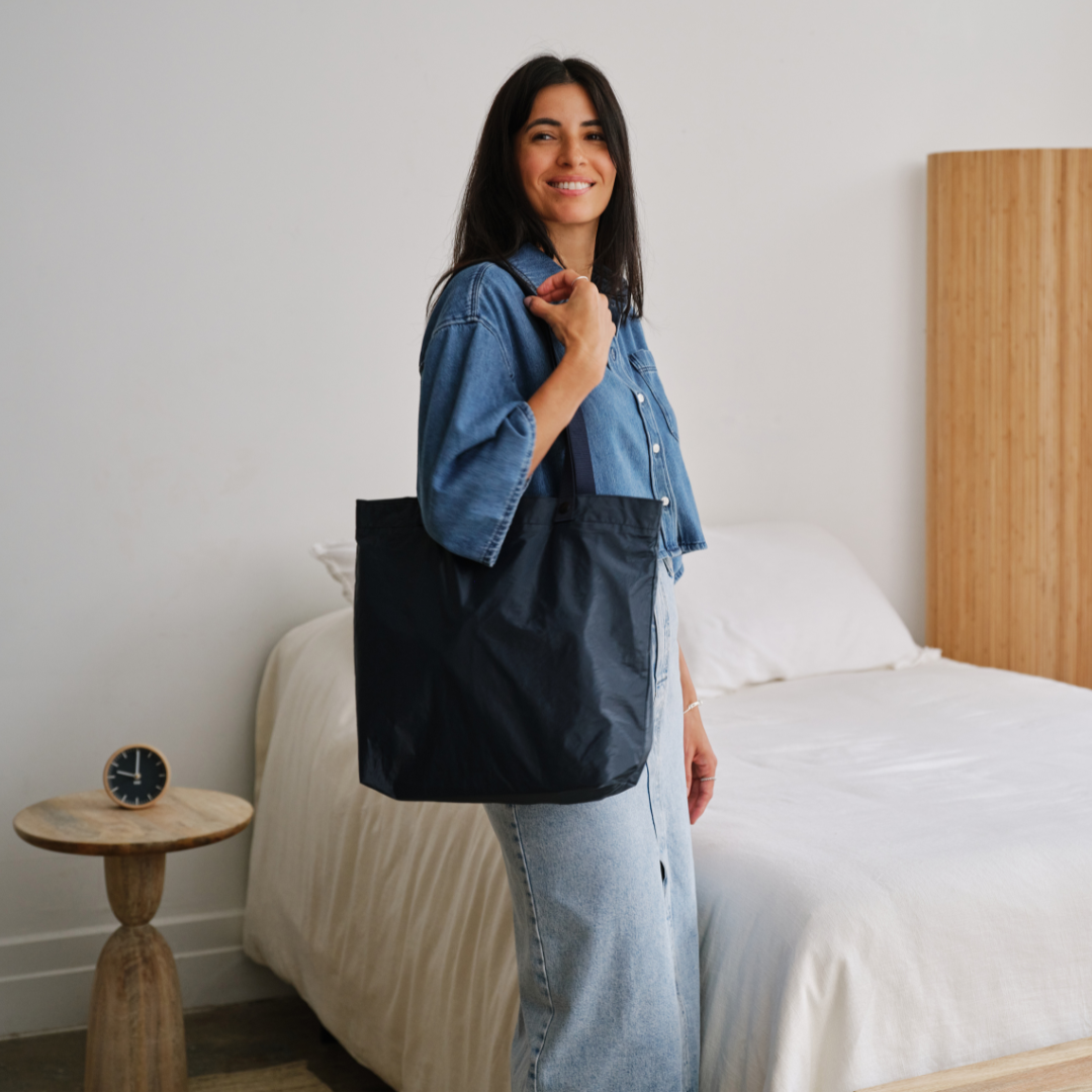 Woman holding a navy blue Lo & Sons Del Mar packable reusable tote bag in a bedroom setting about to run errands