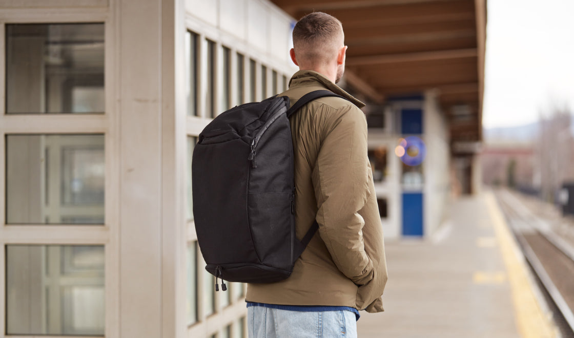 Man with a black backpack standing on a train platform commuting to work and traveling