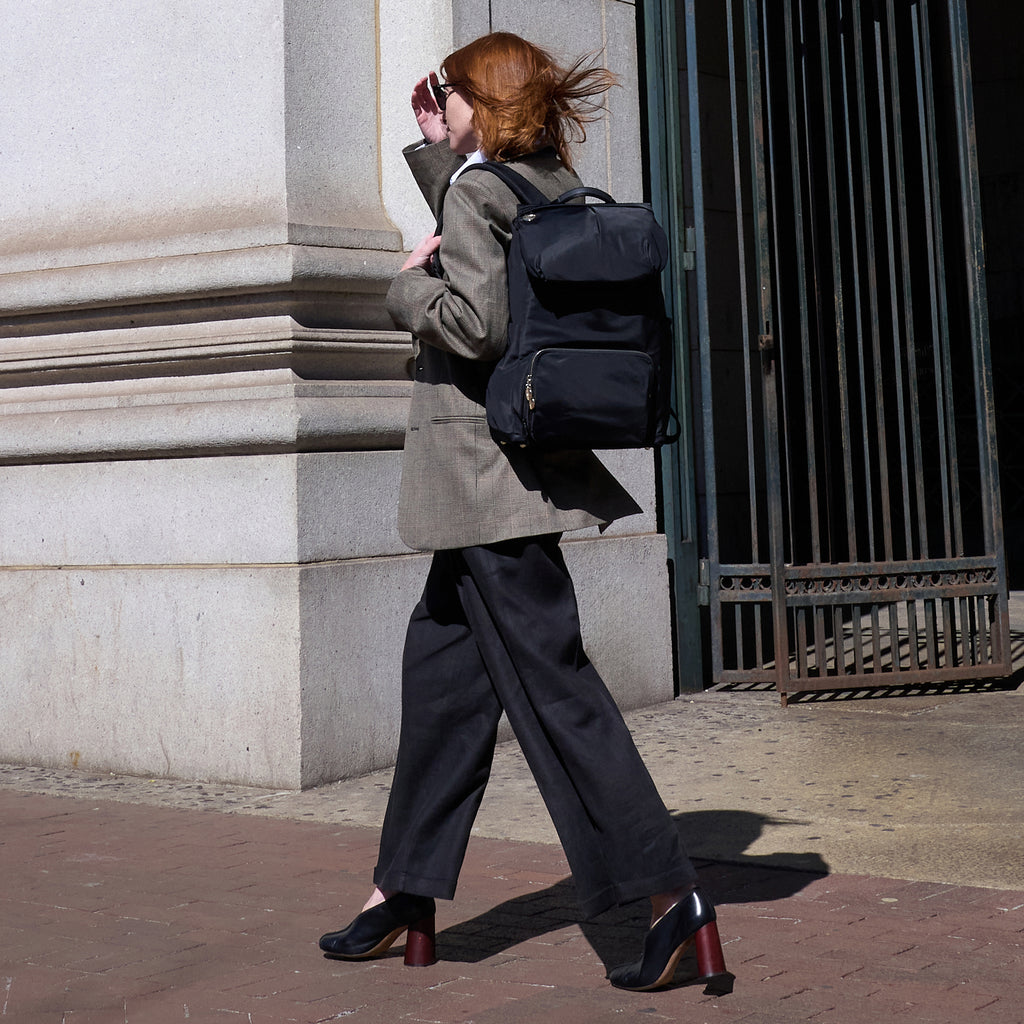 Woman walking down sidewalk in urban setting wearing Lo & Sons Melrose work laptop backpack in nylon