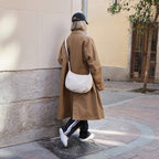 woman wearing trench coat walking down sidewalk carrying the Aoyama 2 in ivory leather as a crossbody bag