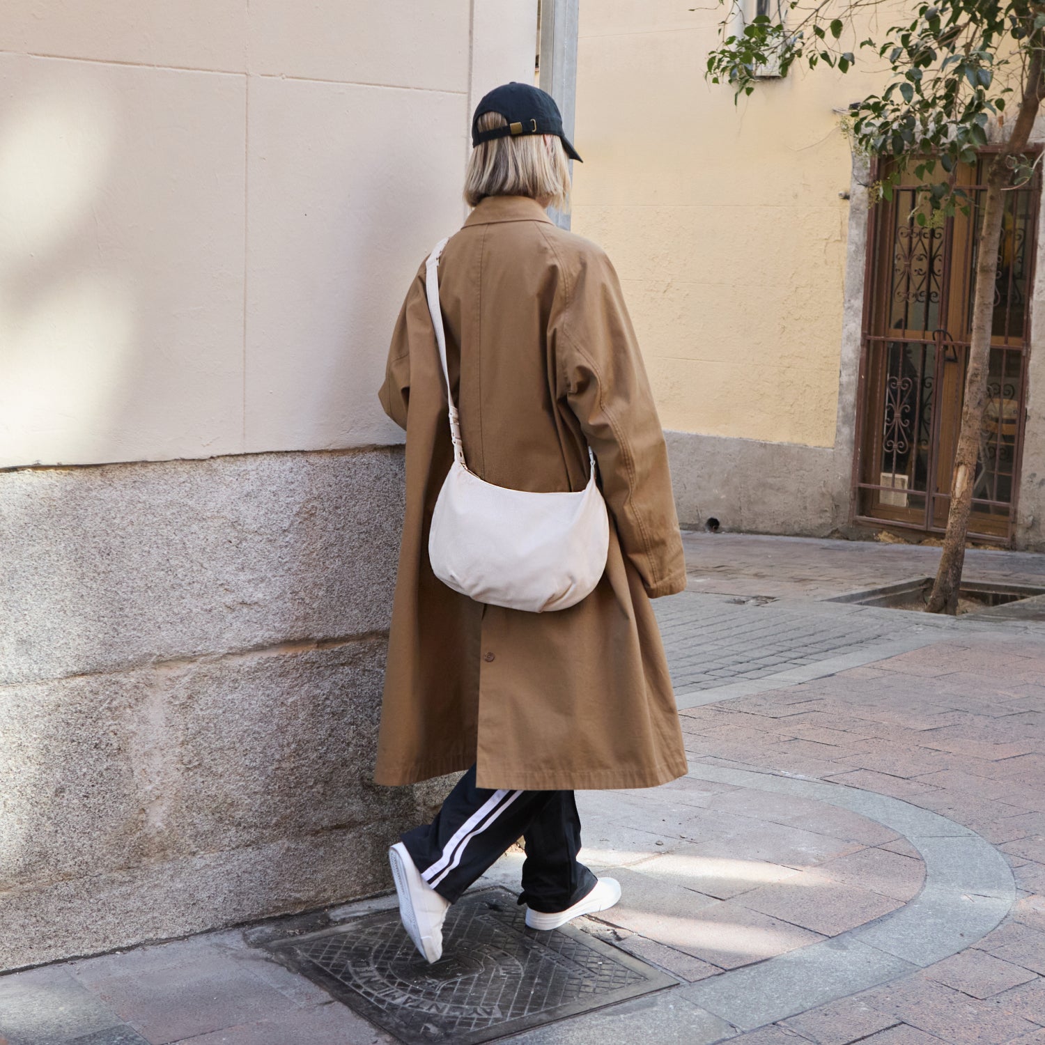 woman wearing trench coat walking down sidewalk carrying the Aoyama 2 in ivory leather as a crossbody bag