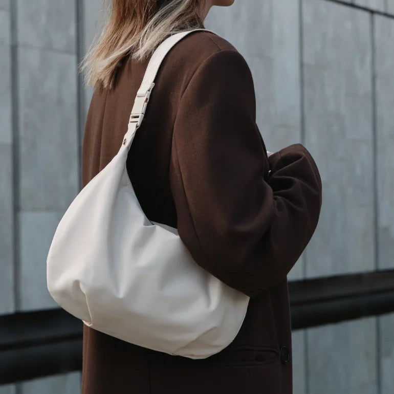 Woman wearing a brown coat with a Lo & Sons white Aoyama bag standing in front of a gray wall
