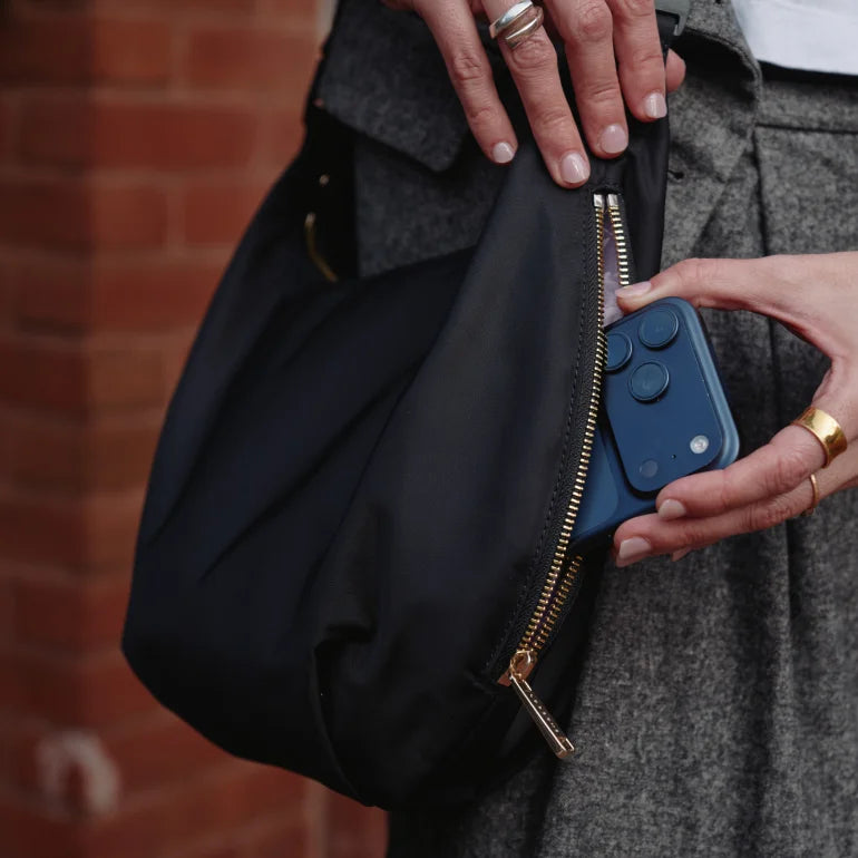 Person opening a black Lo & Sons Aoyama bag in nylon to take out a phone from it's side pocket
