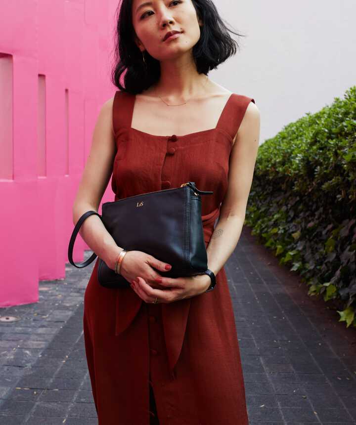 woman in Mexico City in front colorful walls carrying the Lo & Sons Pearl bag as a large wristlet