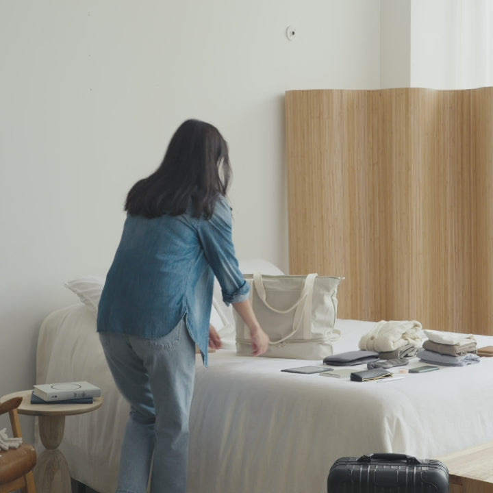 Woman packing Lo & Sons Catalina Deluxe Tote in Dove Grey canvas.