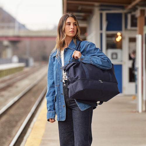 woman carrying the Lo & Sons Catalina Deluxe weekender and duffle bag in deep navy at the train station